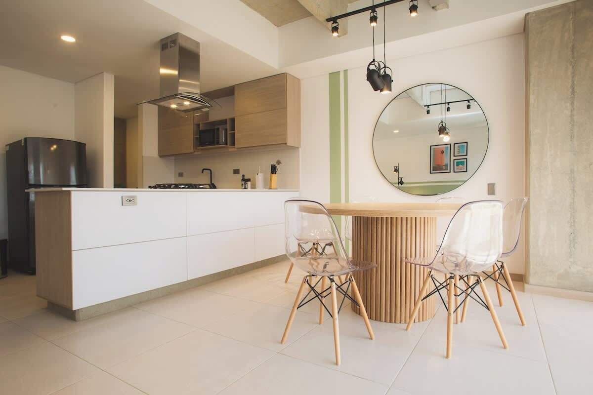 Une cuisine moderne avec un îlot central, des meubles blancs et un grand miroir rond accroché au mur.