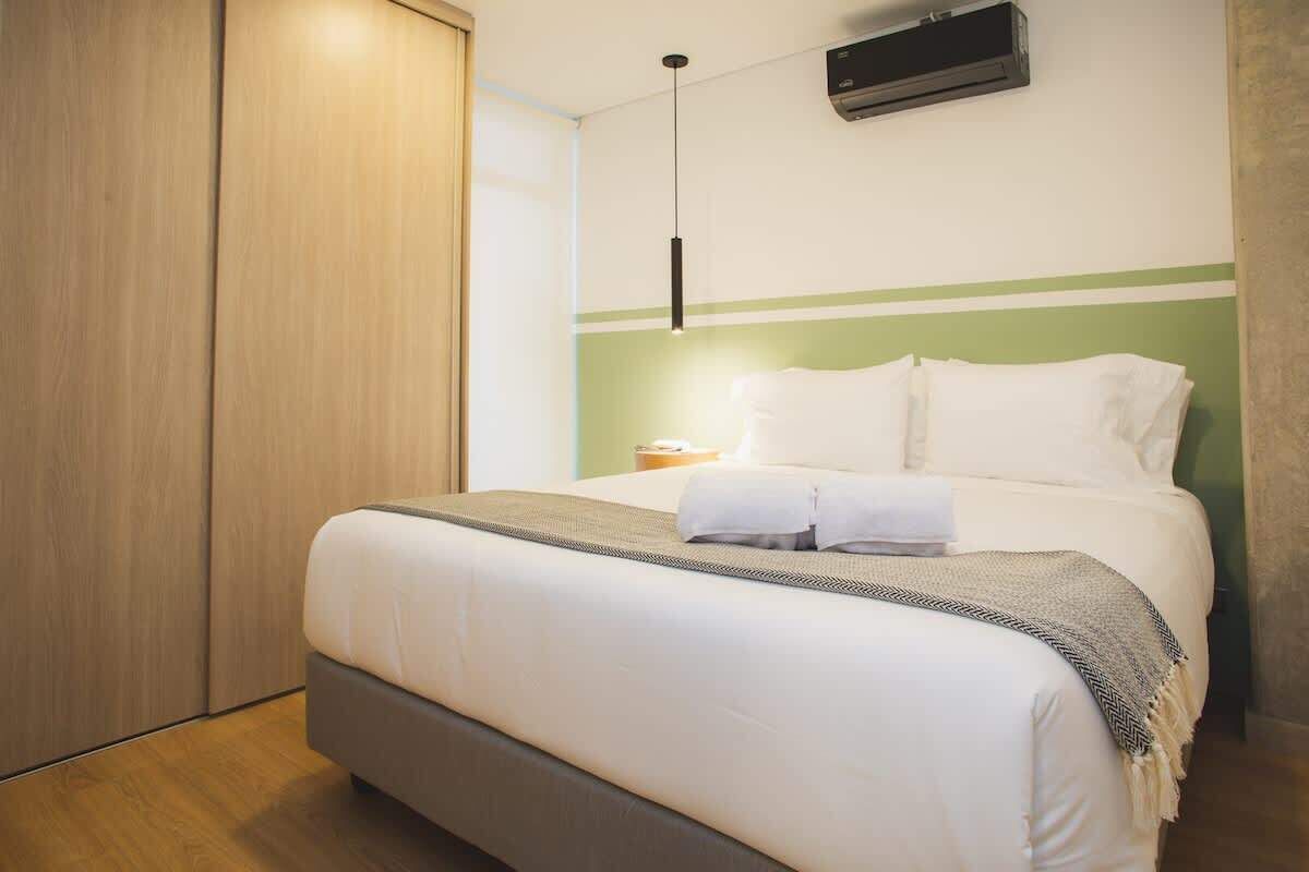 A neatly made bed with white linens and a grey blanket, a bedside table with a lamp, and a wardrobe with sliding doors.