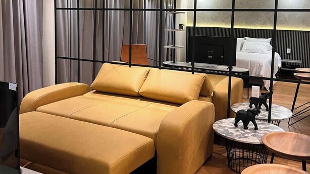 A modern hotel room with a large sofa, a TV, a desk, and a small dining area. - Stunning Studio in Candelaria (Bogotá)