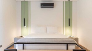 Ein modernes Schlafzimmer mit einem Bett, das zwischen zwei Nachttischen platziert ist, einer Wandklimaanlage und einer Leuchte über dem Bett.
