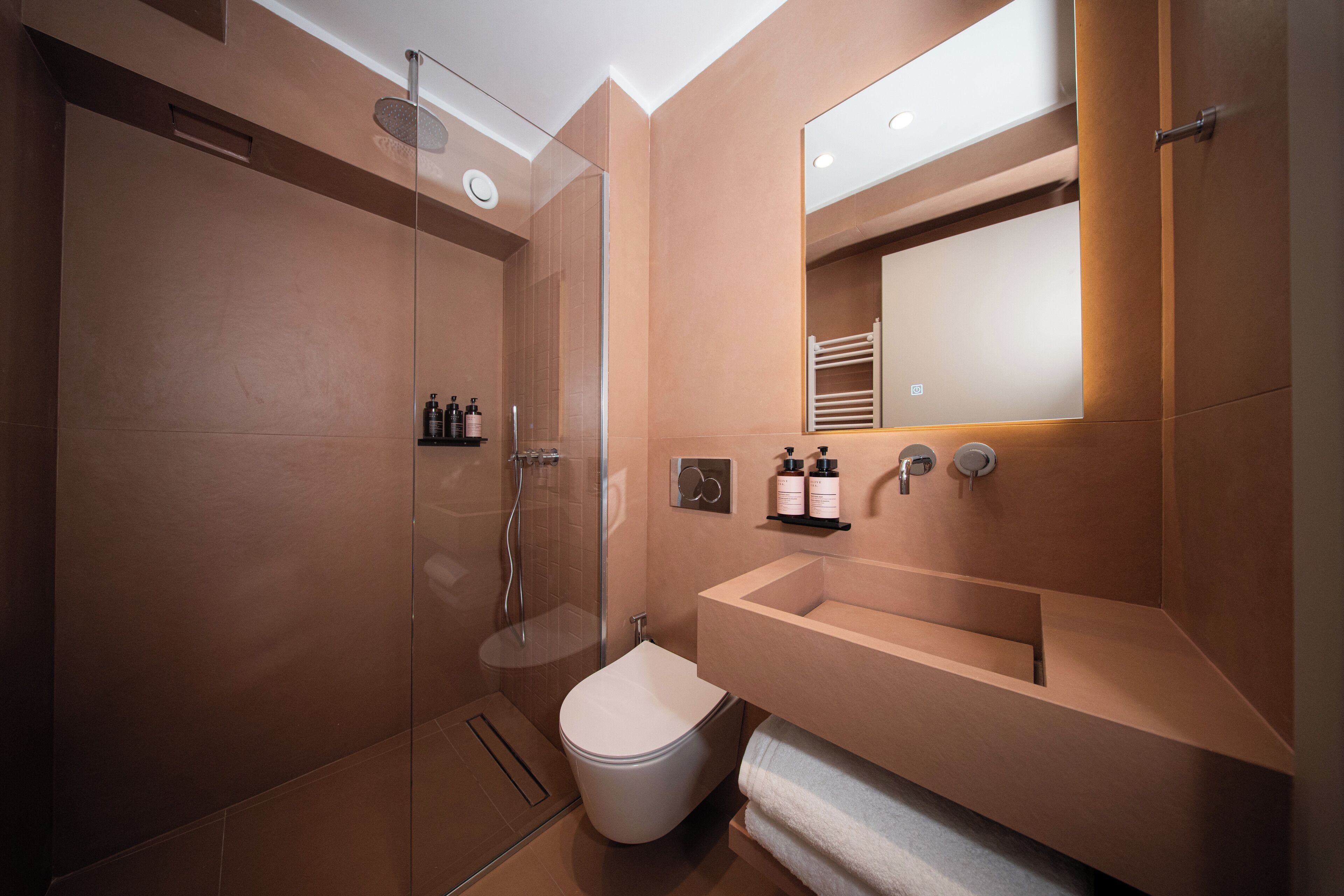 A modern bathroom with a glass-enclosed shower, a white toilet, and a beige sink with a mirror above.