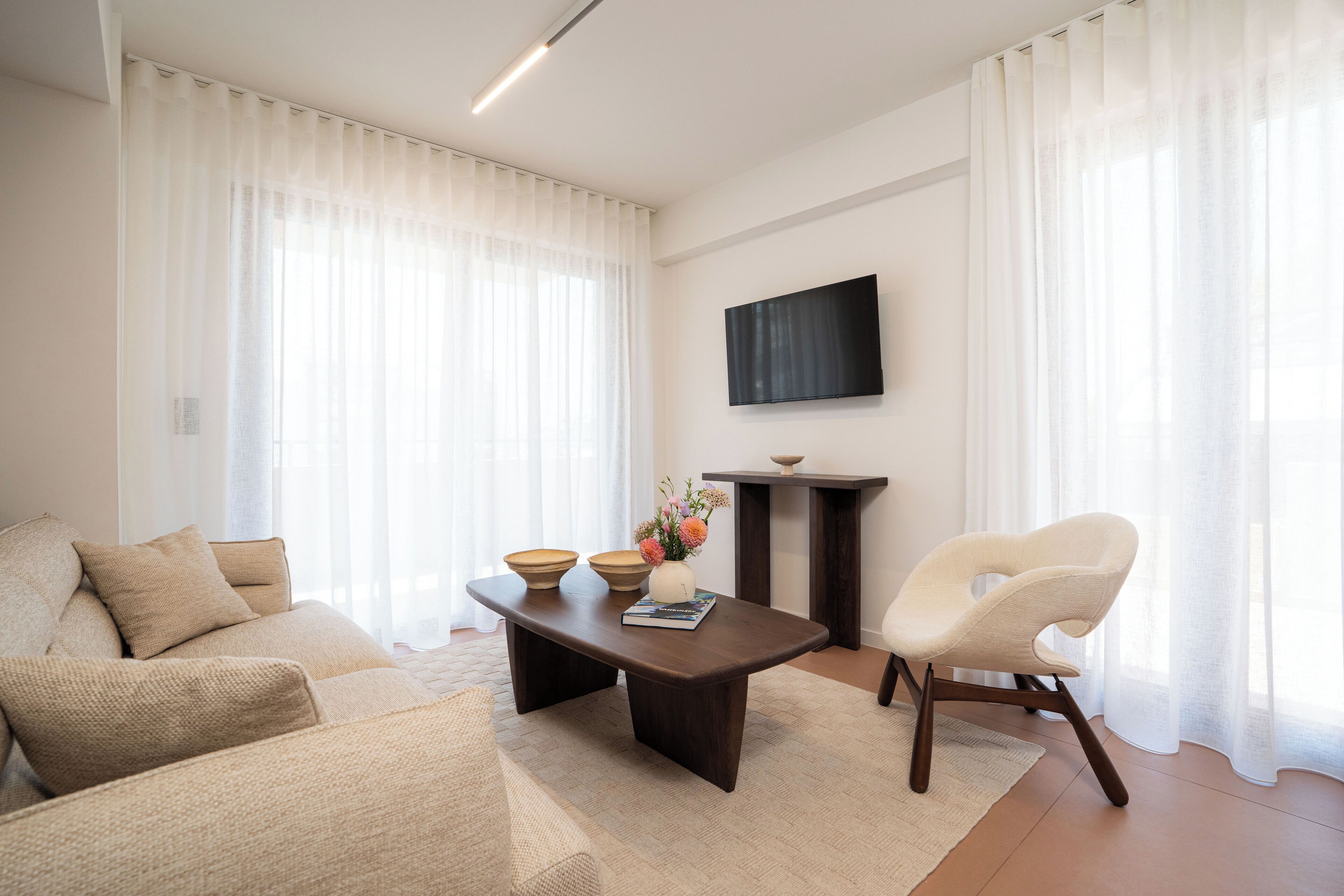 A modern living room with a sofa, a coffee table, a chair, and a flat-screen TV mounted on the wall.