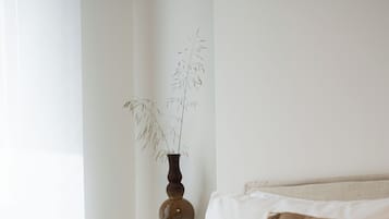 A neatly made bed with white and brown bedding, a vase with dried plants on the nightstand, and a lamp.