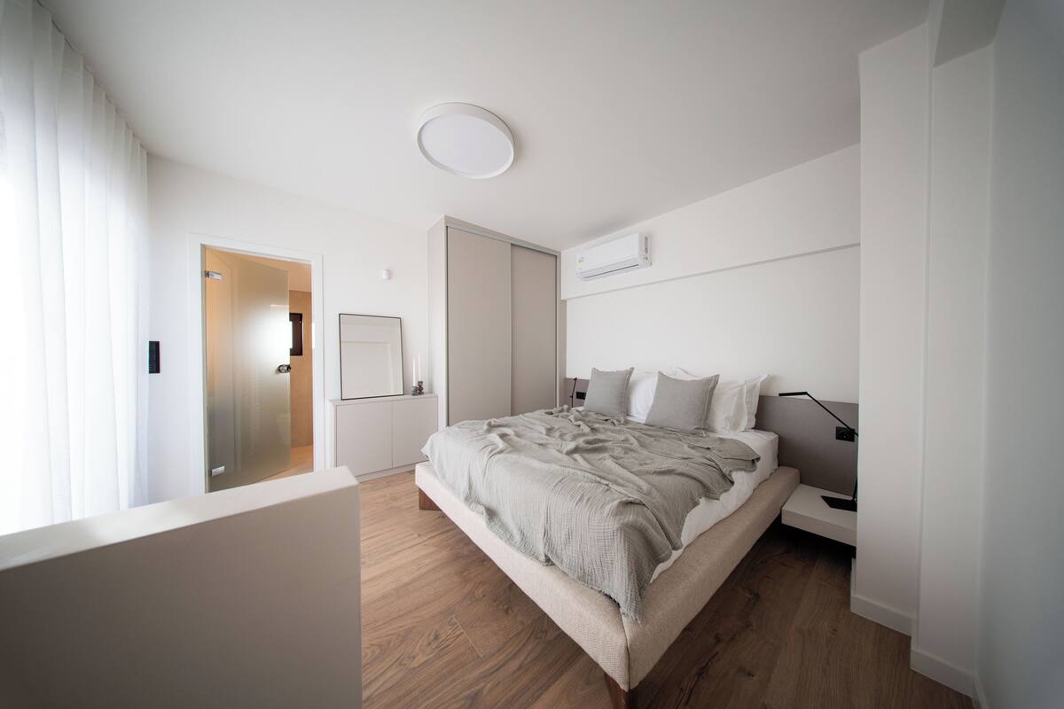 Quarto moderno com uma cama grande, mesas de cabeceira, uma luminária de teto e um aparelho de ar condicionado.