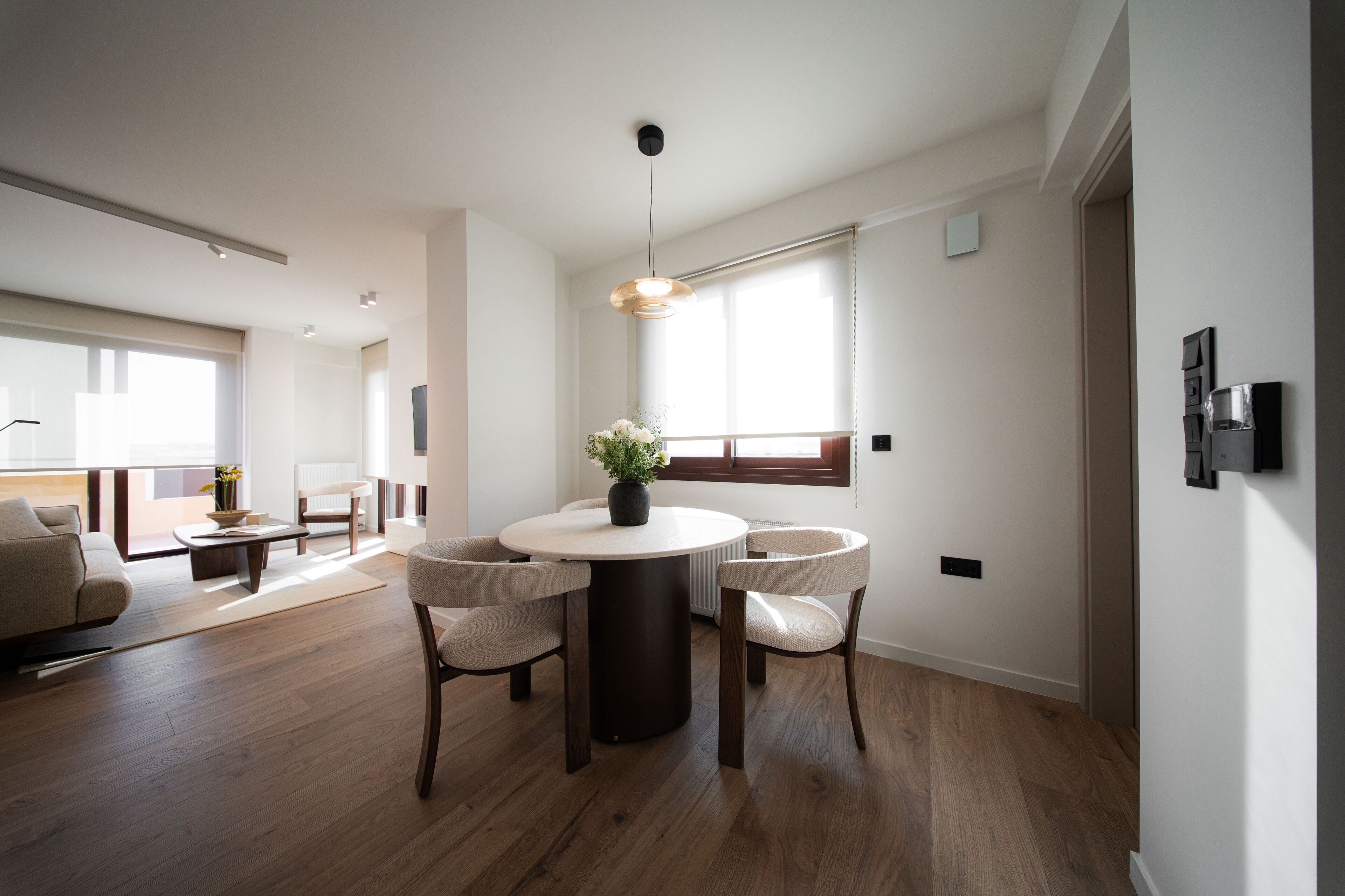 A modern dining area with a round table, four chairs, a potted plant, and a pendant light.