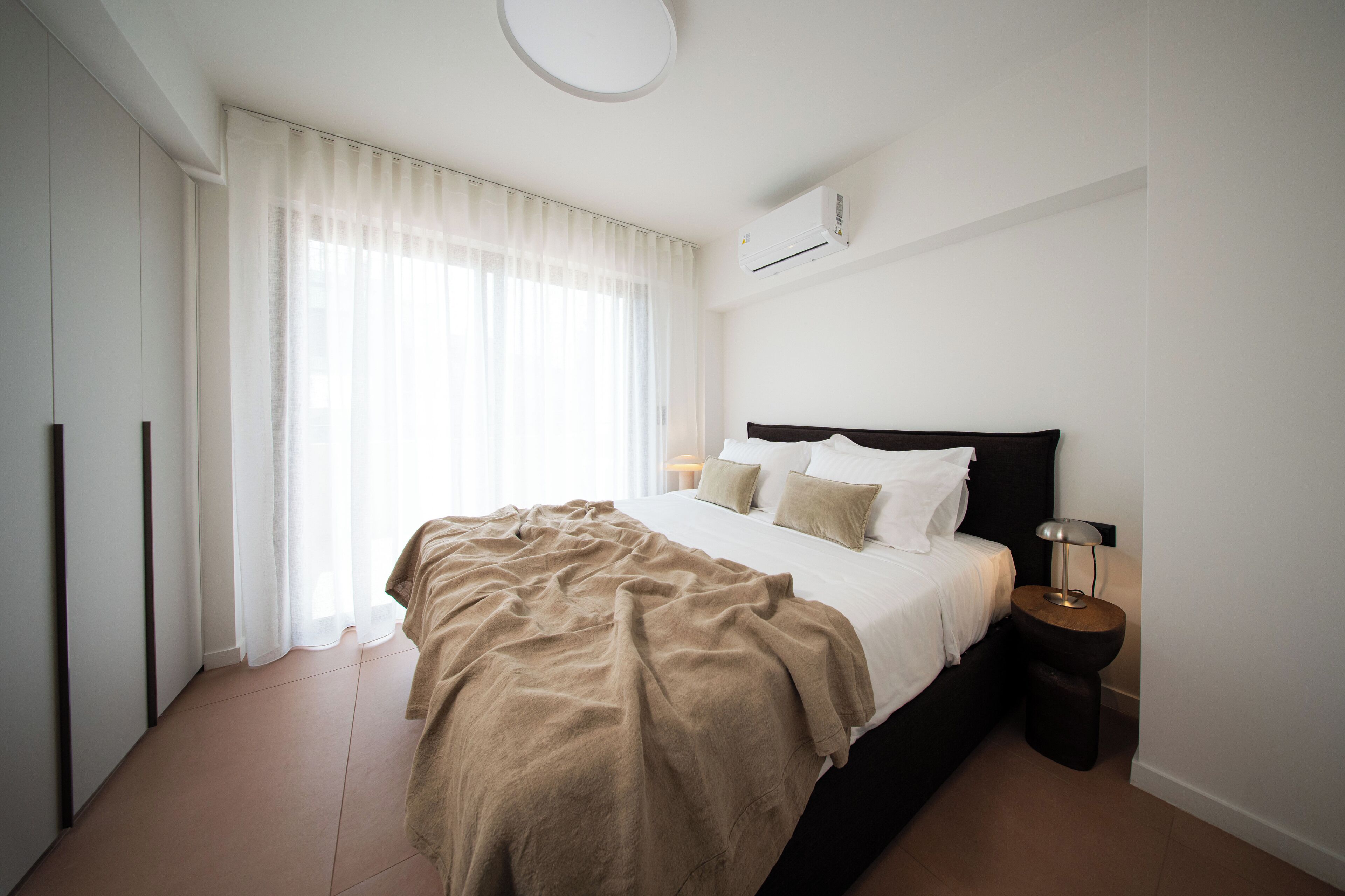 Une chambre à coucher avec un lit, une table de chevet, une lampe et une fenêtre avec des rideaux.