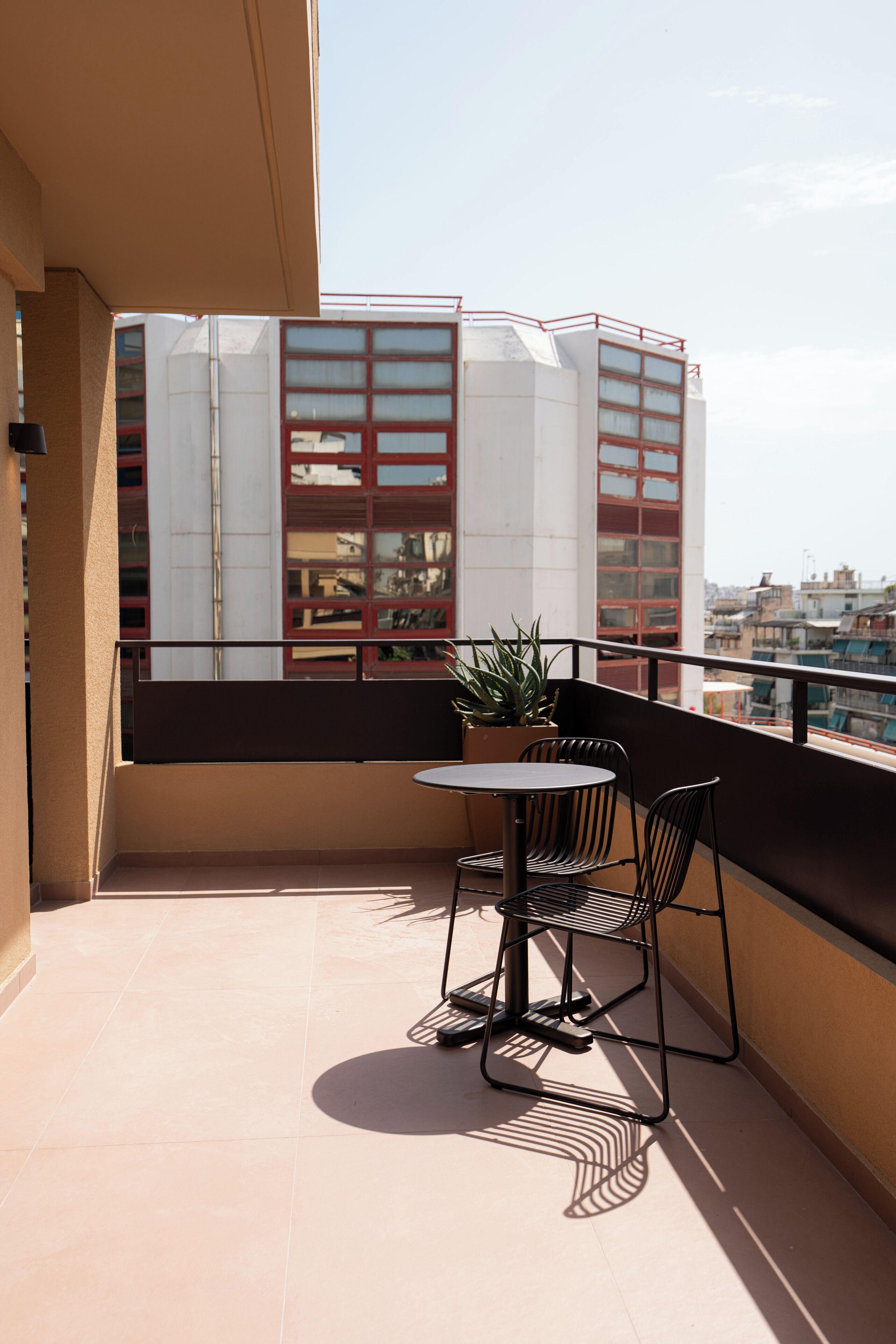 A balcony with a small table and chairs, a potted plant, and a view of buildings.