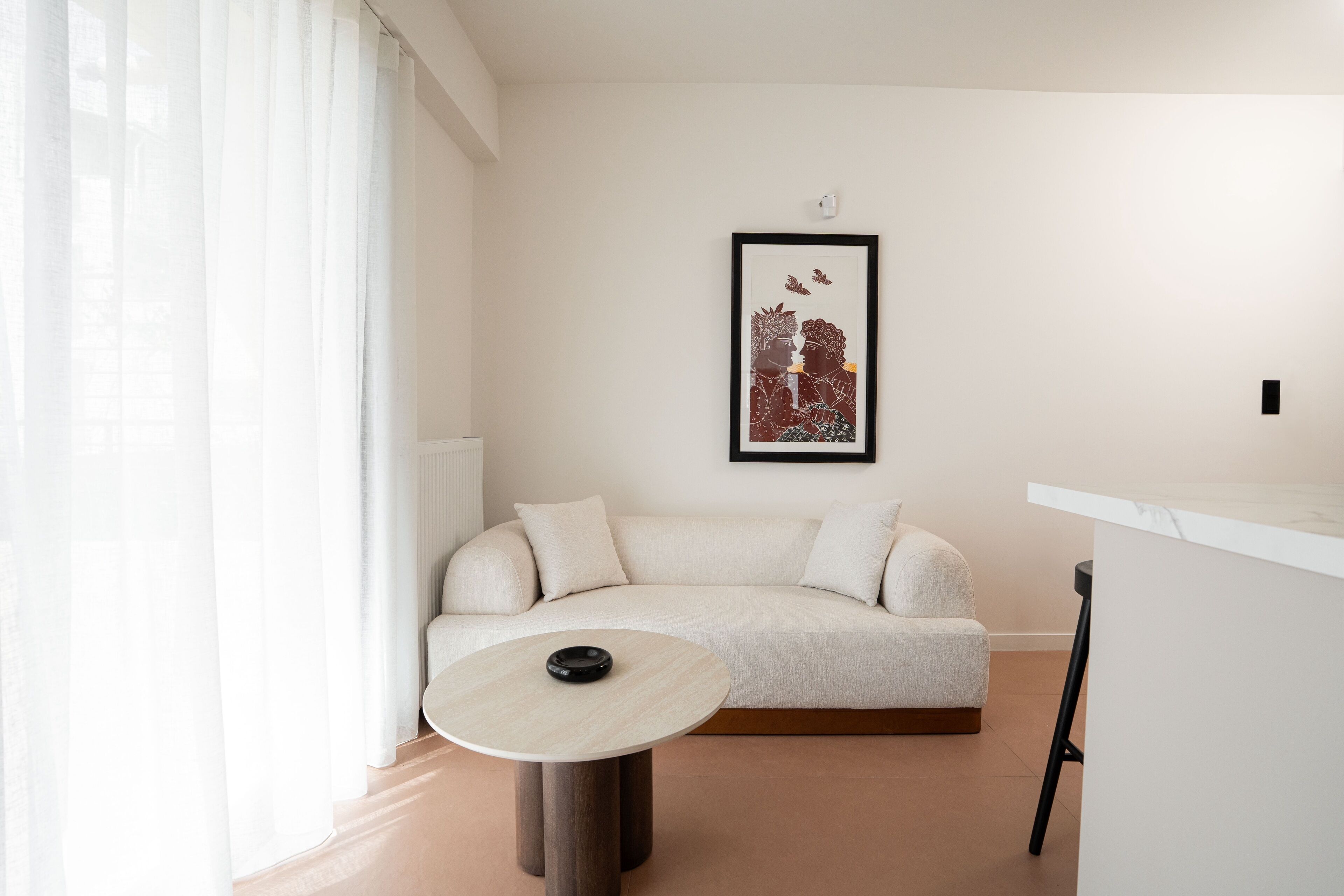 A modern living room with a beige sofa, a round table, and a framed artwork on the wall.