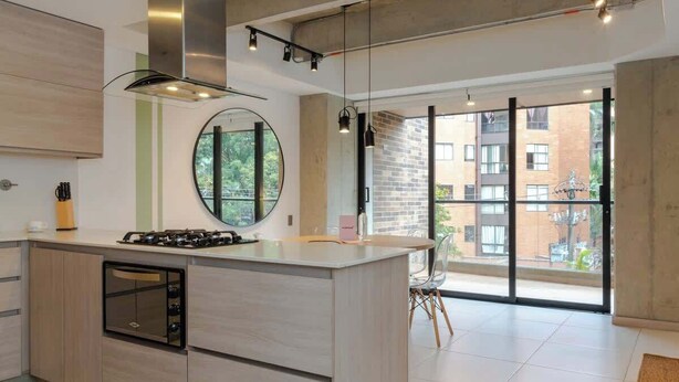 Een moderne keuken met een centraal eiland, inbouwapparatuur en grote ramen met uitzicht op de omgeving.