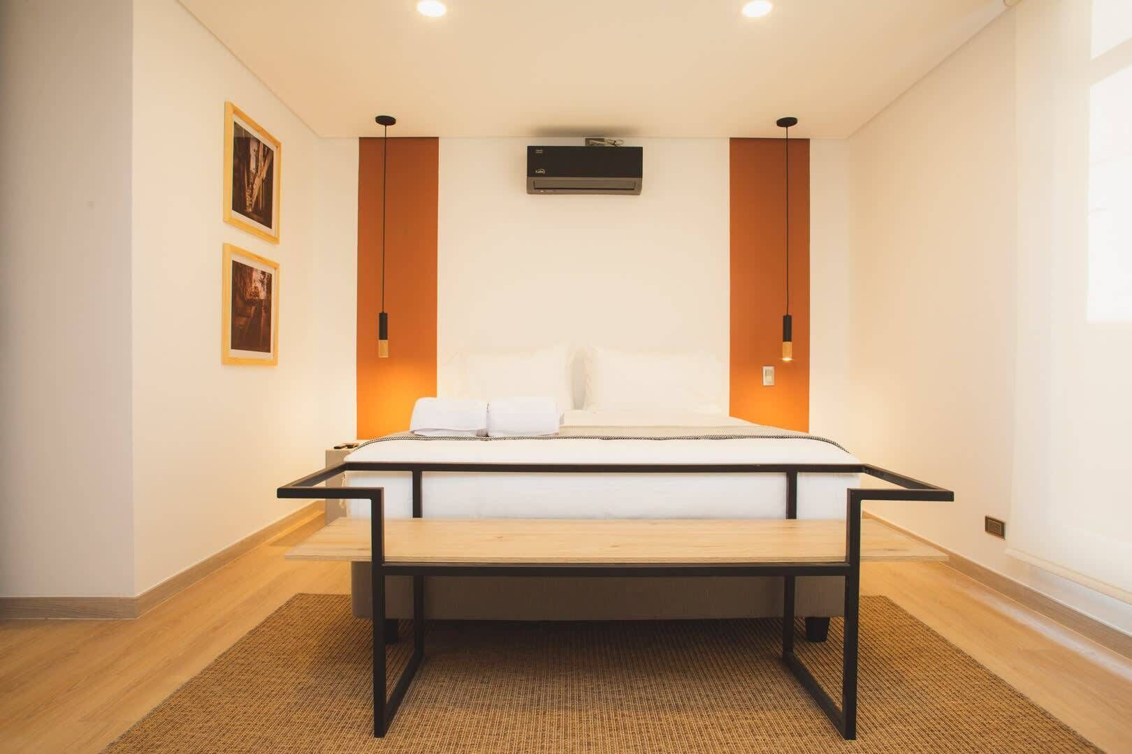 Quarto moderno com cama, escrivaninha e cadeira. Há duas unidades de ar condicionado e duas luminárias fixadas na parede.