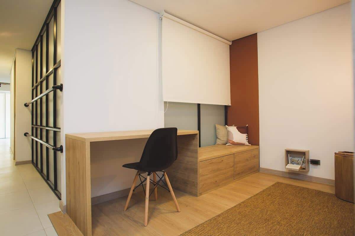 A modern room with a wooden desk, black office chair, and a built-in bench with cushions.