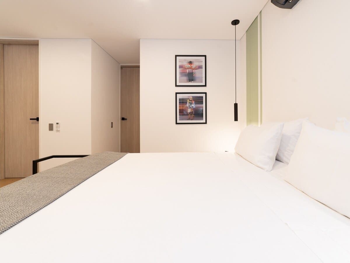 A modern bedroom with a large bed, a wooden door, and two framed pictures on the wall.