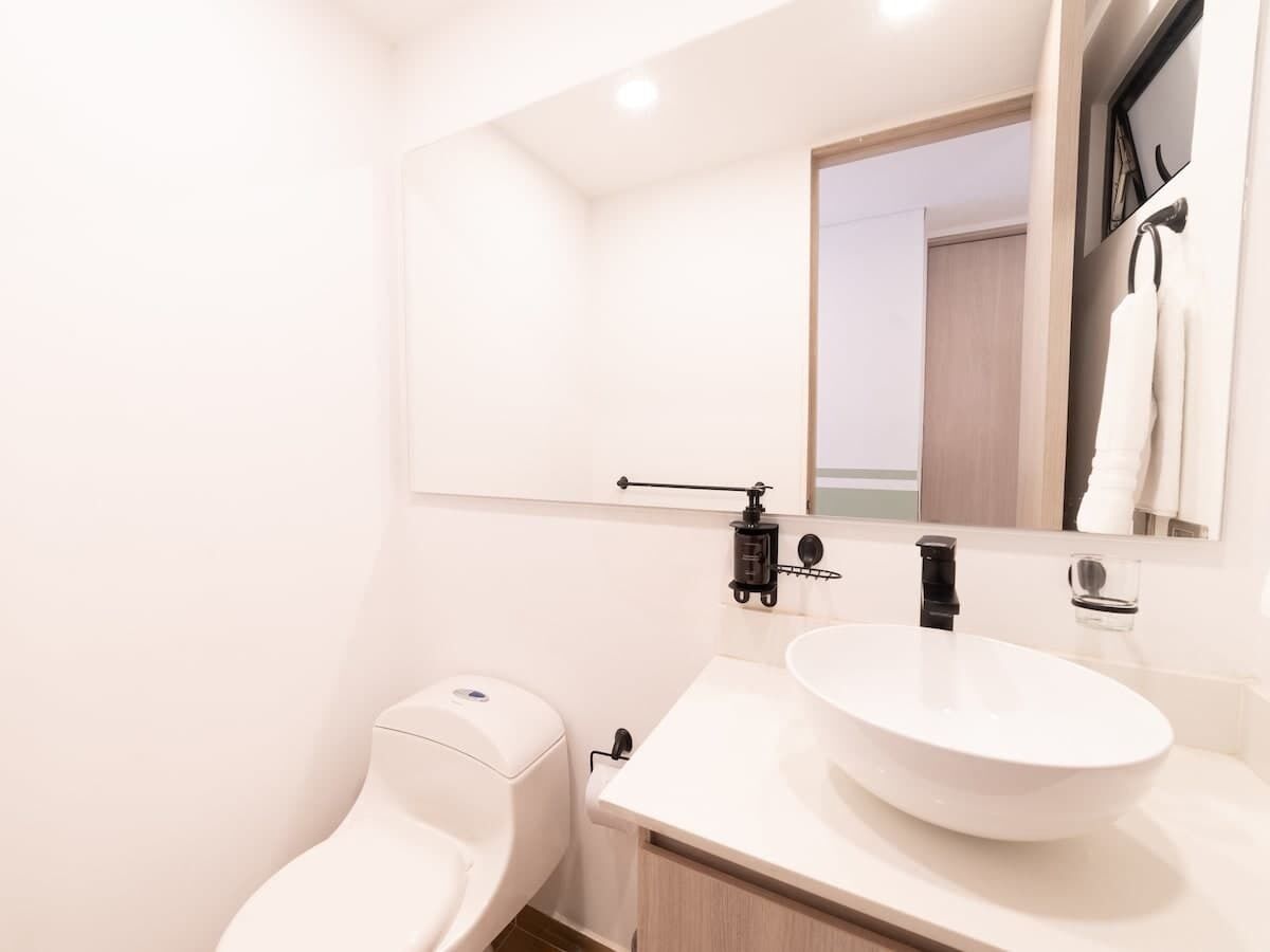 Un bagno moderno con il water bianco, un lavandino bianco e uno specchio sopra il lavandino.