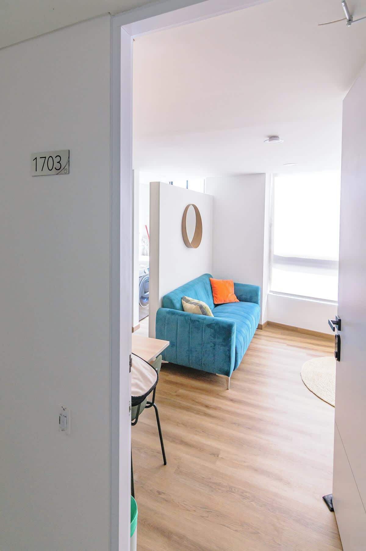 Ein moderner, gut beleuchteter Raum mit einem blauen Sofa, einer runden Wanddekoration und Holzboden.