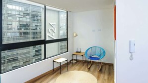 Una habitación moderna con un ventanal grande, una mesita, una silla y una alfombra tejida.
