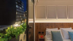 Et moderne hotelværelse med en stor seng, et natbord og udsigt til bybilledet om natten.
