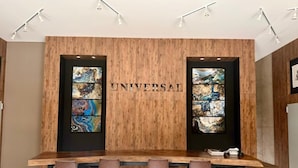 Et moderne barområde med en trævæg, to store vinduer med abstrakt kunst, samt et langt barbord med stole.