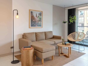 A modern living room with a sectional sofa, a round wooden coffee table, a floor lamp, and a framed cityscape painting.
