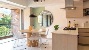 A modern kitchen with a round dining table, white chairs, a hanging light fixture, and a view of greenery outside. - Perfect 3 BR w/ Balcony in Laureles Medellín (Medellín)