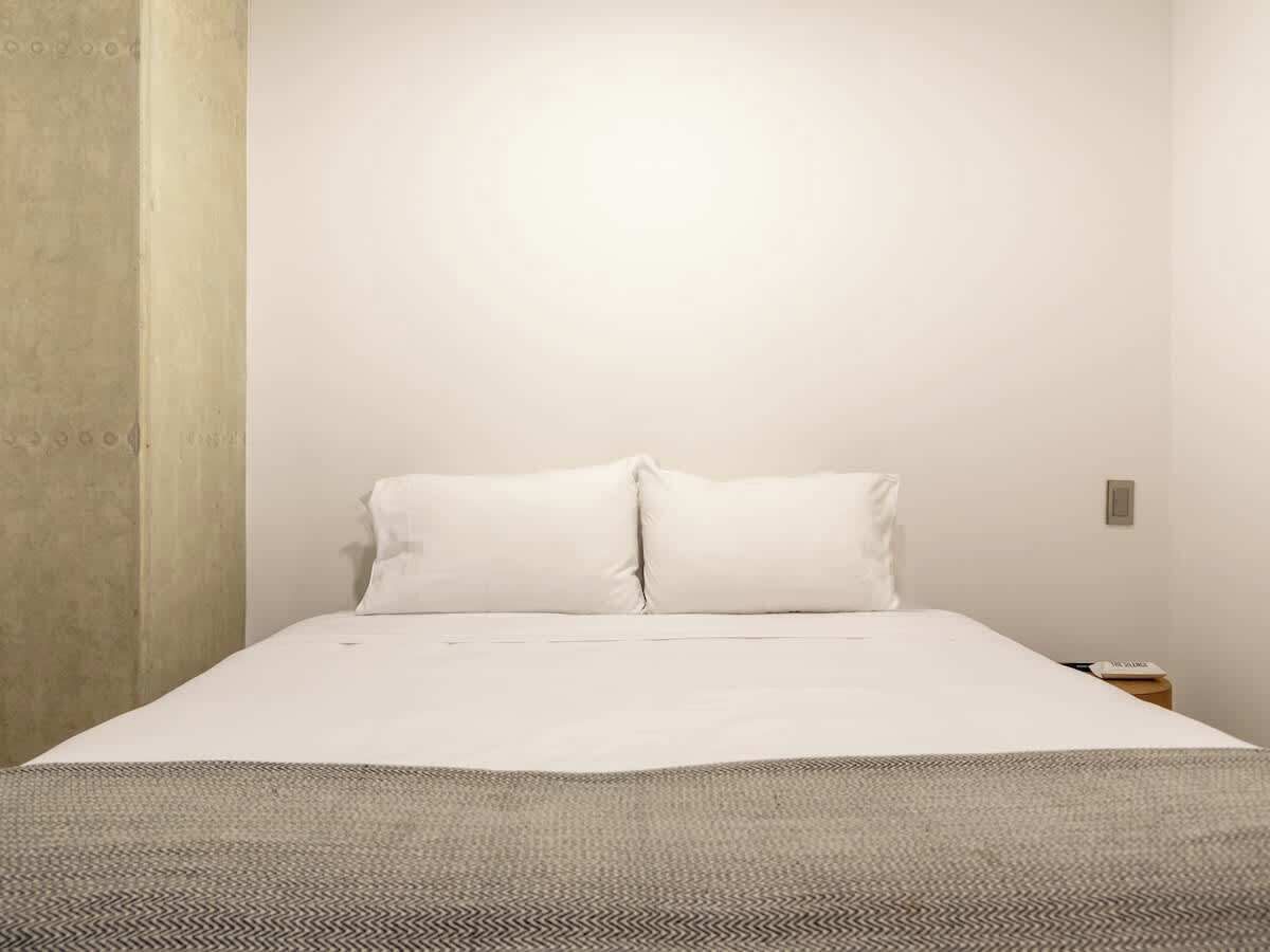Una habitación sencilla y limpia con una cama, una mesita de noche y una pared lisa.