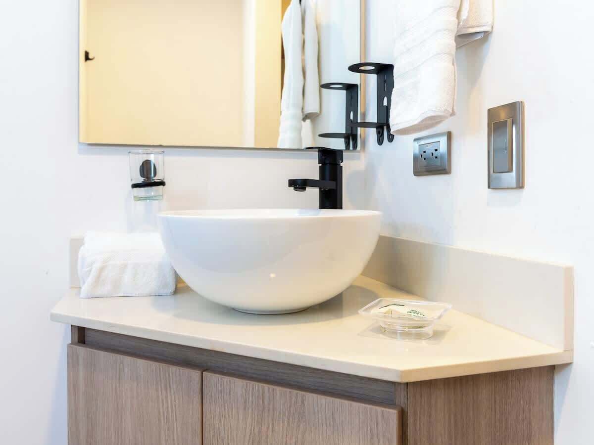 A modern bathroom with a large white vessel sink, a mirror, and a towel rack.