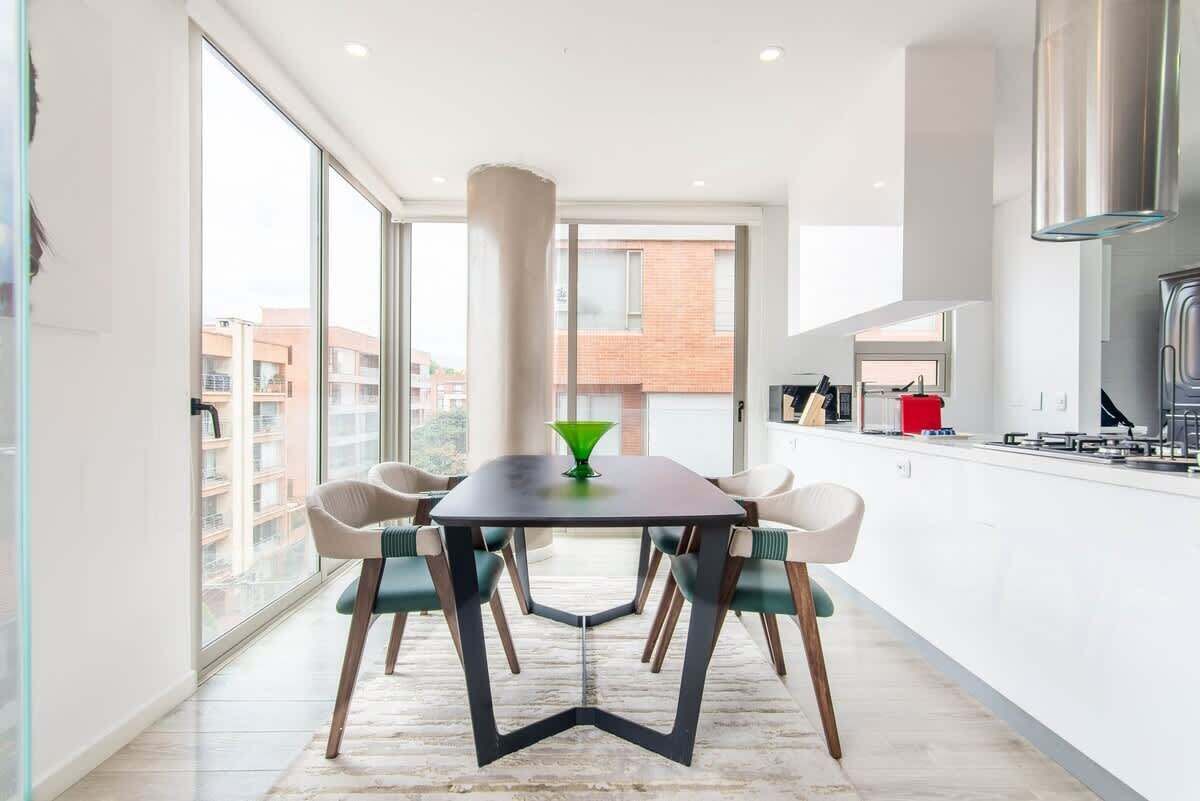 A modern kitchen with a dining area, large windows, and a view of buildings.