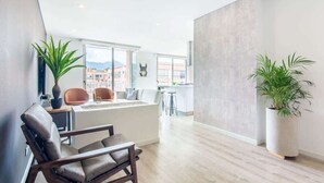 A modern living room with a sofa, chairs, a dining table, and a large potted plant. - Modern Apartment in Usaquien (Bogotá)