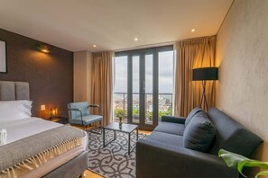 A hotel room with a bed, a sofa, a chair, a small table, and a large window with curtains. - Amazing Studio in Candelaria - La Primera 416 (Bogotá)