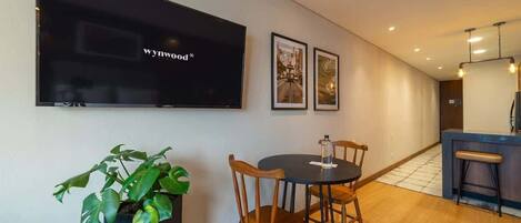 A modern dining area with a round table, wooden chairs, a potted plant, a flat-screen TV mounted on the wall, and framed pictures.