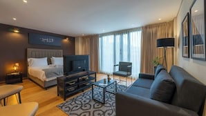 Ein modernes Hotelzimmer mit Bett, Sofa, Fernseher und Couchtisch.