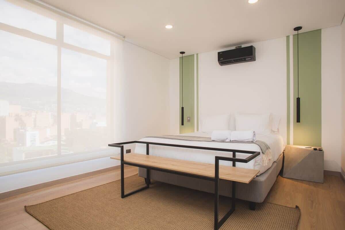 A modern bedroom with a bed, a bench, and a view of the city.