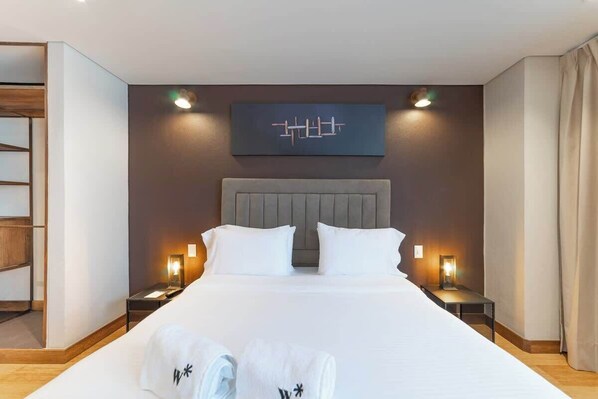 Une chambre d’hôtel moderne avec un grand lit, deux tables de chevet et une œuvre d’art accrochée au mur.