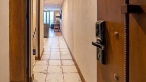 Un couloir avec une porte en bois, un sol carrelé en pierre et une vue sur une pièce comprenant un coin repas.