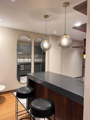 A modern kitchen with a central island, two bar stools, and pendant lighting. - Lovely Studio in Candelaria (Bogotá)