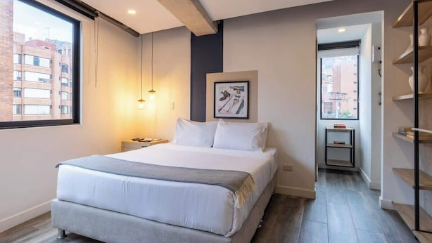 A modern bedroom with a large bed, a bedside table, a hanging light, and a framed picture on the wall. - Amazing Loft in Chapinero (Bogotá)