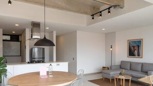 Ein moderner Wohnraum mit einem runden Holzes Esstisch, transparenten Stühlen, einem grauen Sofa und einem kleinen Beistelltisch.
