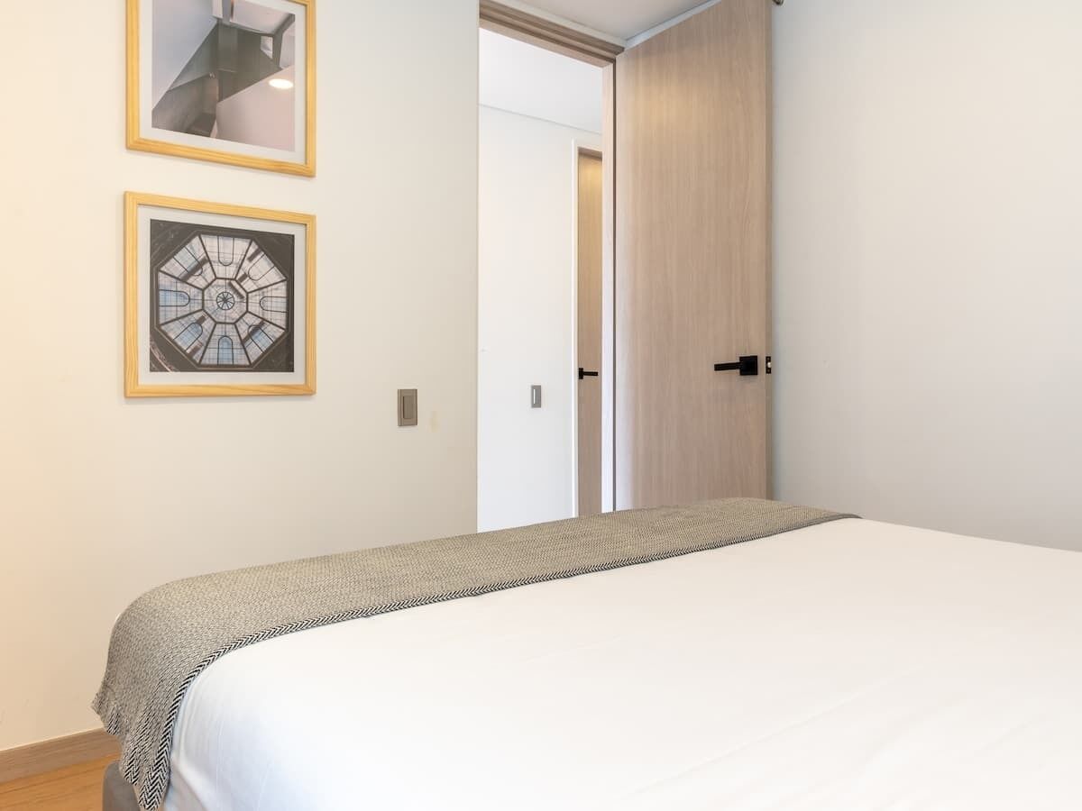 Ein Schlafzimmer mit einem Bett, einer Tür und zwei gerahmten Bildern an der Wand.