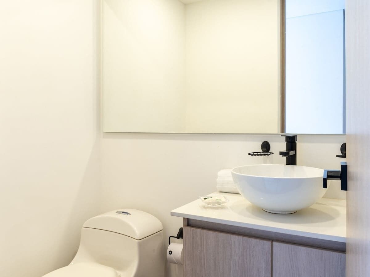 A modern bathroom with a white toilet, a large white basin sink, and a mirror above the sink.