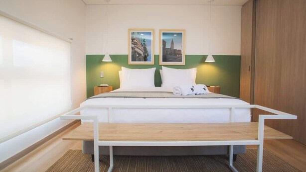 A modern hotel room with a large bed, two bedside tables, a bench at the foot of the bed, and two wall-mounted lamps. - Splendid Studio in Laureles in Medellín (Medellín)