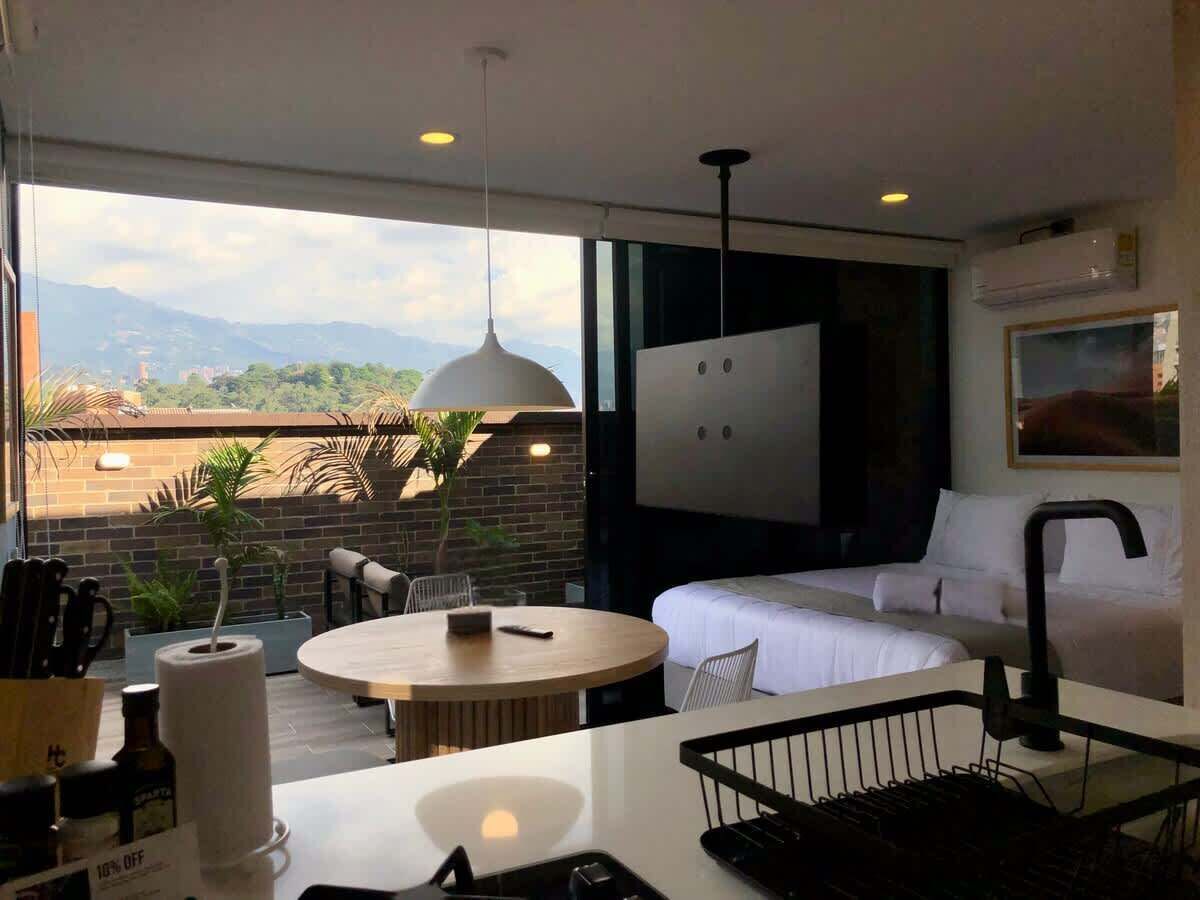A modern hotel room with a balcony, a round dining table, a sofa, and a bed.