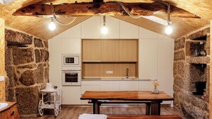 A rustic kitchen with stone walls, wooden beams, and a wooden table with benches. - House in the Gerês area (4840-070)