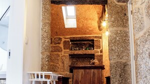 A stone-walled room with a fireplace, a white chair, and a small dog statue. - House in the Gerês area (4840-070)