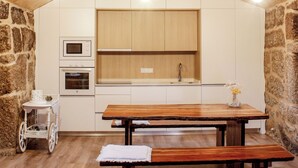 A rustic kitchen with wooden beams, a stone wall, and a wooden dining table. - House in the Gerês area (4840-070)