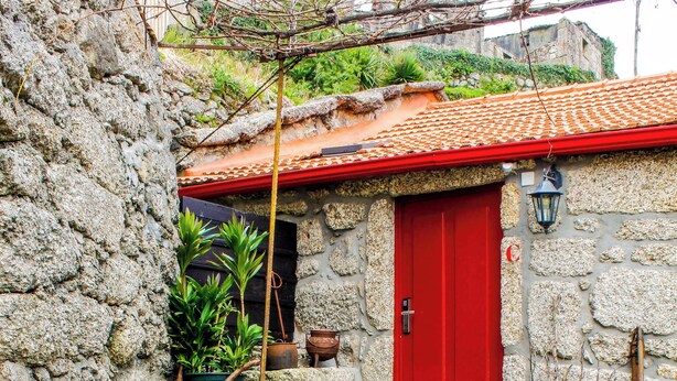 A rustic outdoor seating area with wooden tables and chairs, a red door, and stone walls. - House in the Gerês area (4840-070)