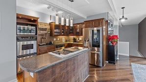 Una cocina moderna con electrodomésticos de acero inoxidable, armarios de madera e iluminación colgante.