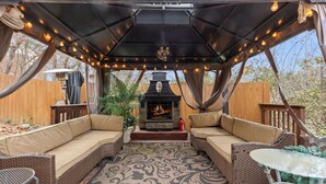 Un patio al aire libre con mobiliario de mimbre, una mesa de vidrio y una chimenea.