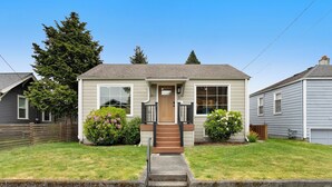 A single-story house with a front porch, a small front yard, and a wooden fence. - Charming 3-bedroom Craftsman with AC + EV-Charger + very walkable in Ballard (Seattle)