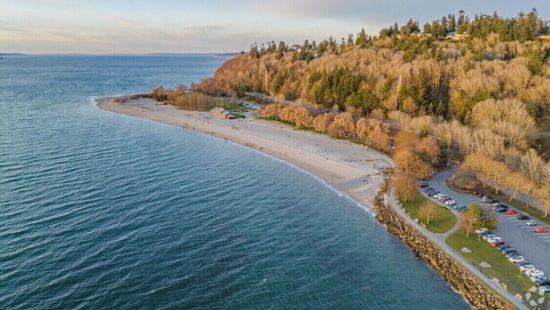 An aerial view of a coastal area with a beach, parking lot, and a forested hillside. - Charming 3-bedroom Craftsman with AC + EV-Charger + very walkable in Ballard (Seattle)