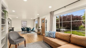 A modern living room with a sofa, armchair, and dining area with chairs and a table. - Charming 3-bedroom Craftsman with AC + EV-Charger + very walkable in Ballard (Seattle)