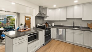 A modern kitchen with white cabinets, stainless steel appliances, and a large island. - Charming 3-bedroom Craftsman with AC + EV-Charger + very walkable in Ballard (Seattle)